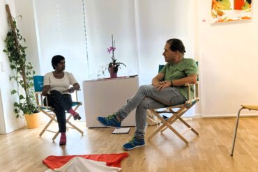 Die Galeristin Krishna-Sara Helmle und der Künstler Thomas Mautner-Hipp sitzen sich in der Kunstgalerie gegenüber.